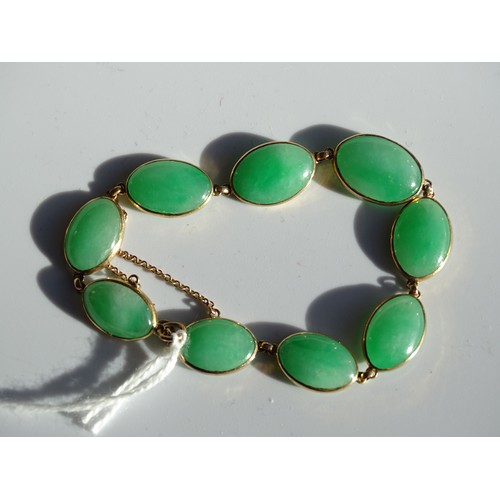 545 - A bracelet of nine oval jade cabochons in gold spectacle mounts, (unmarked, tests as 14k approximate... 