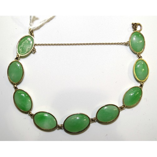 545 - A bracelet of nine oval jade cabochons in gold spectacle mounts, (unmarked, tests as 14k approximate... 