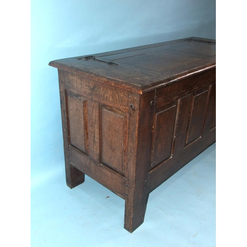 100 - An antique oak panelled coffer, the lift lid above plain fielded panels and stiles extended to form ... 