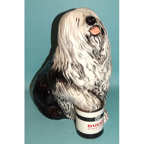 A ceramic fireside figure of the Dulux dog, with front paw resting on a tin of Dulux paint, 33cm high, (probably Beswick but no factory mark).