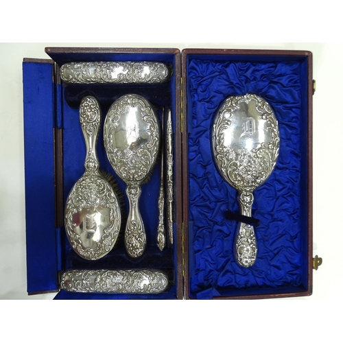 182 - A cased seven-piece silver-mounted dressing table set embossed with flowers with etched letter 'D', ... 