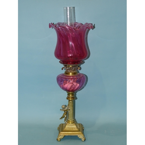 138 - A late-19th century oil lamp, the cranberry glass reservoir on brass reeded column with applied wing... 