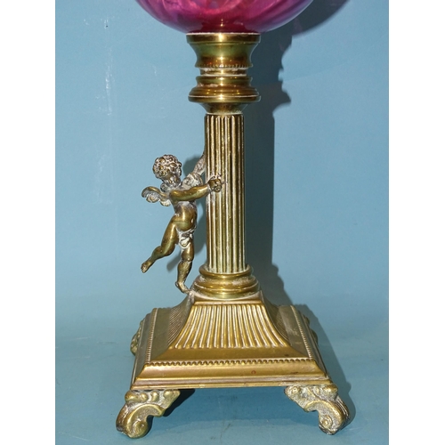 138 - A late-19th century oil lamp, the cranberry glass reservoir on brass reeded column with applied wing... 