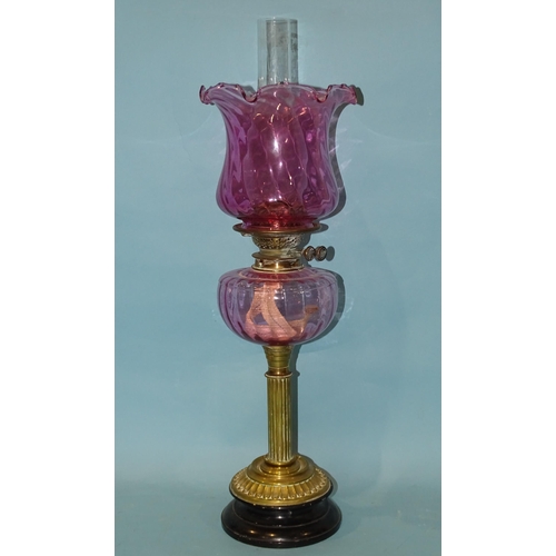 139 - A late-19th century oil lamp, the cranberry glass reservoir on brass reeded column and circular foot... 