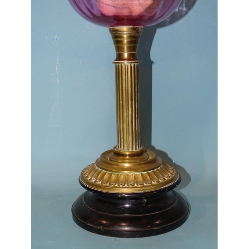 139 - A late-19th century oil lamp, the cranberry glass reservoir on brass reeded column and circular foot... 