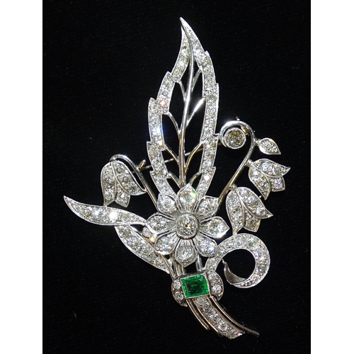 A large diamond and emerald spray brooch millegrain-set a rectangular emerald amidst old brilliant-cut diamond-set flowers and foliage, total diamond weight estimated at 5.2cts, emerald approximately 0.7cts, in unmarked white metal setting, (tested and valued as 14ct white gold), 8.2 x 5.5cm, 23.4g.