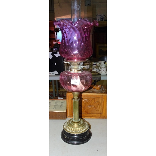 134 - A late-19th century oil lamp, the cranberry glass reservoir on brass reeded column and circular foot... 