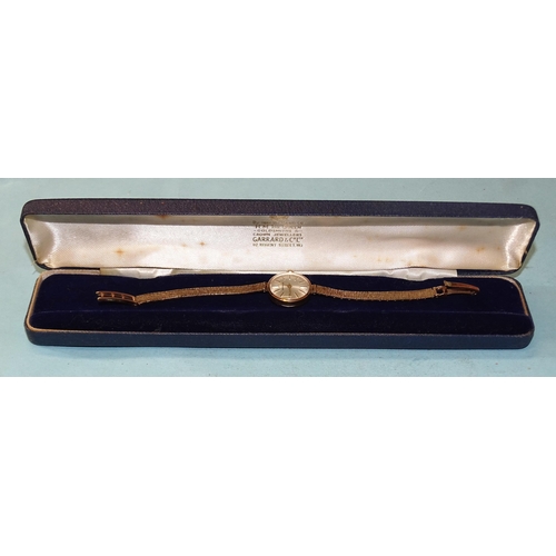 301 - Garrard, a 1980's lady's 9ct gold wrist watch, the circular silver dial with baton numerals, in gold... 