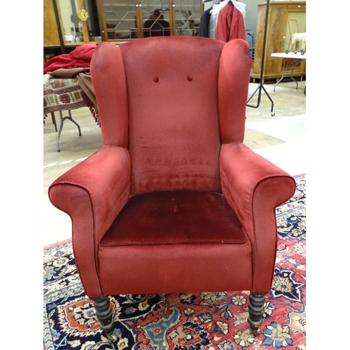 2 - A late Victorian upholstered wing armchair on ebonised front legs.