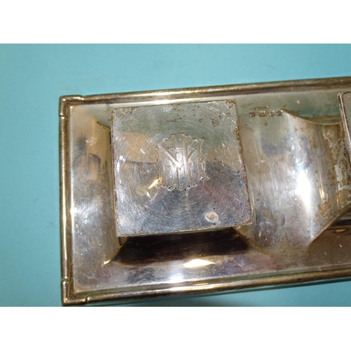 512 - A George V silver inkstand of rectangular form, on loaded base, fitted with two hinged lidded inkwel... 