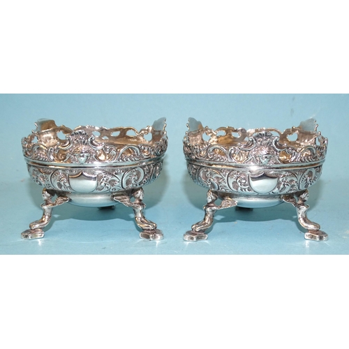 533 - A pair of late-Victorian silver salts with embossed and pierced scroll decoration, raised on three w... 