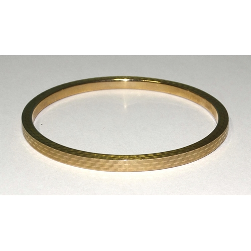 833 - A 9ct gold slave bangle with engine-turned decoration, 78mm inner diameter, 10g.