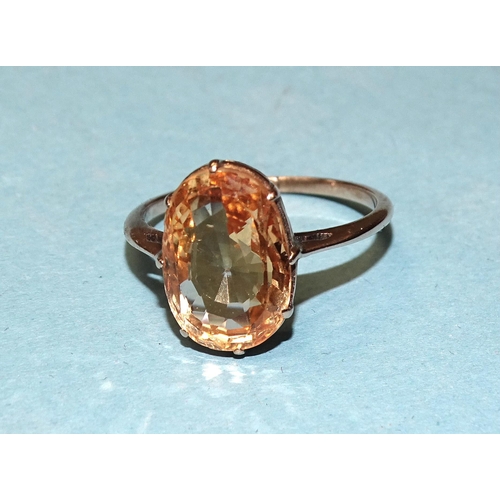 909 - An unmarked gold ring claw-set an oval peach-pink sapphire of approximately 5.4cts, (gold tested as ... 