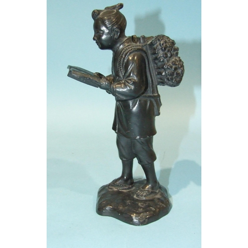 29 - A Japanese bronzed metal figure of a man carrying corn sheafs and reading a book, 19cm high.... 