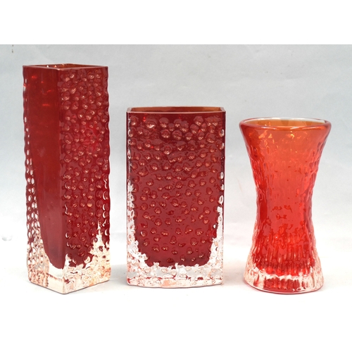 Geoffrey Baxter for Whitefriars, a textured nailhead square-form cased vase in the ruby red colourway, 5.5cm square, 19.5cm high, a bowed nailhead vase in the same colourway, 16cm high, with 9809 paper pattern sticker to base, (small chip to one corner) and a ruby red 'bark' textured hourglass cased vase, 15cm high, (3).
