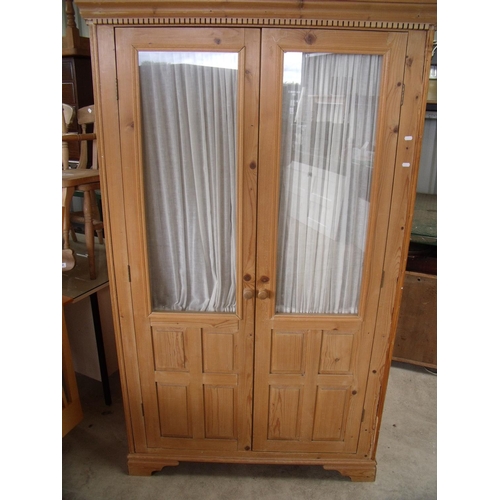 370 - Waxed pine wardrobe enclosed by two glazed and panelled cupboard doors (width 113cm)