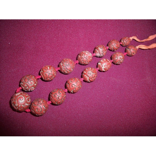 62 - 19th/20th C carved cinnabar lacquer ball necklace, the balls of graduating size on woven silk work s... 