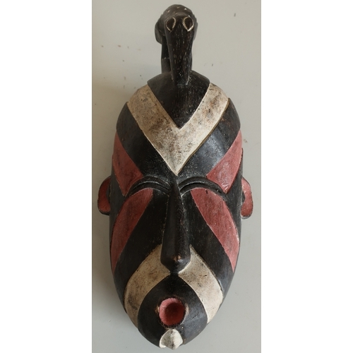 94 - Unusual carved tribal style face mask with white, black and red stripe detail, crested with a figure... 