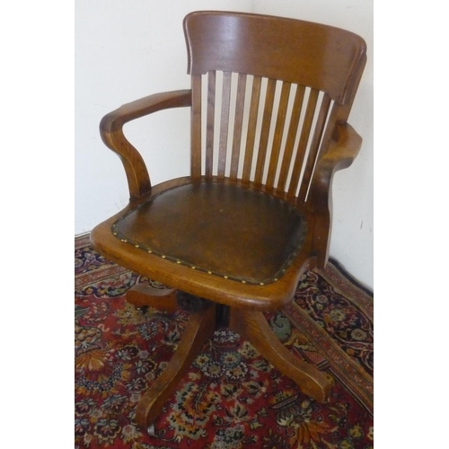 60 - 20th C oak office chair, with curved top rail, slat back and brass nailed rexine seat on four shaped... 
