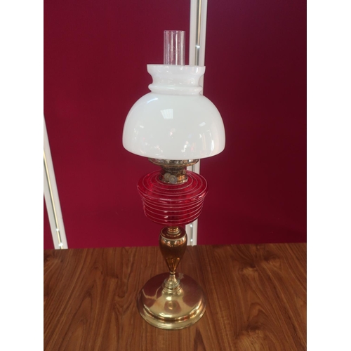 459 - Early 20th C brass oil lamp, with red glass reservoir and clear glass shade, on urn shaped column an... 