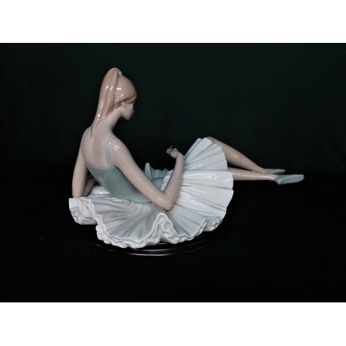 73 - Porcelain figure depicting a resting ballerina holding a flower, H25cm L45cm.