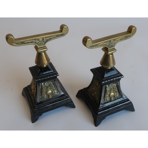 1255 - Pair of Arts and Crafts brass and cast iron fire dogs, scrolled tops on tapering column, the stepped... 