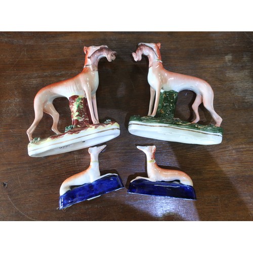 693 - Two Staffordshire models of standing greyhounds with hares in mouth on painted shaped gilt lined bas... 