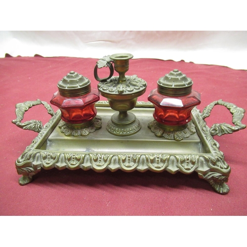 149 - Ornate brass pen and ink stand with two cranberry glass inkwells with brass covers and a central ewe... 