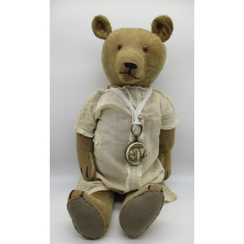 148 - Early American teddy bear with glass eyes and non-working growler mechanism, wearing a white dress a... 