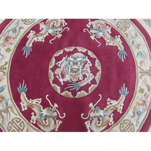 346 - C20th circular Chinese embossed washed woolen rug, claret ground with central dragon motif surrounde... 