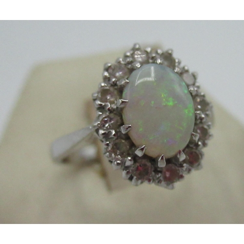 1129 - Hallmarked 18ct white gold ring with central oval opal and a halo of twelve round cut diamonds, by P... 