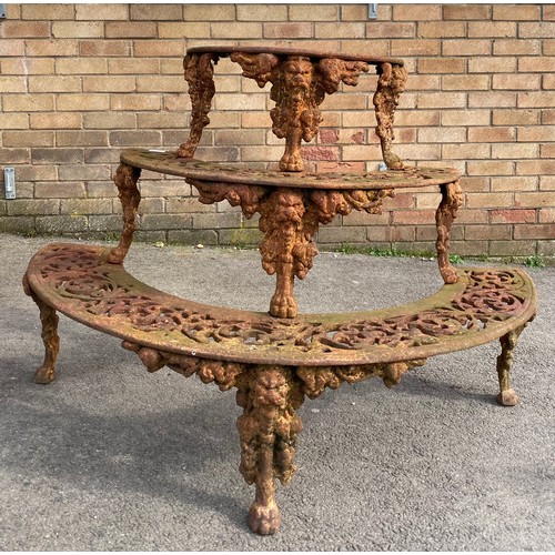 1596 - Cast iron demi-lune plant stand, three pierced graduated tiers on mask head and paw supports, W117cm... 