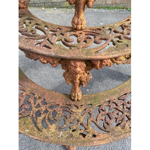 1596 - Cast iron demi-lune plant stand, three pierced graduated tiers on mask head and paw supports, W117cm... 