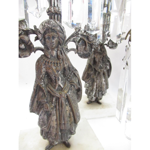 228 - Garniture of three silvered metal candelabra, figural bases with urn sconces on white marble bases, ... 