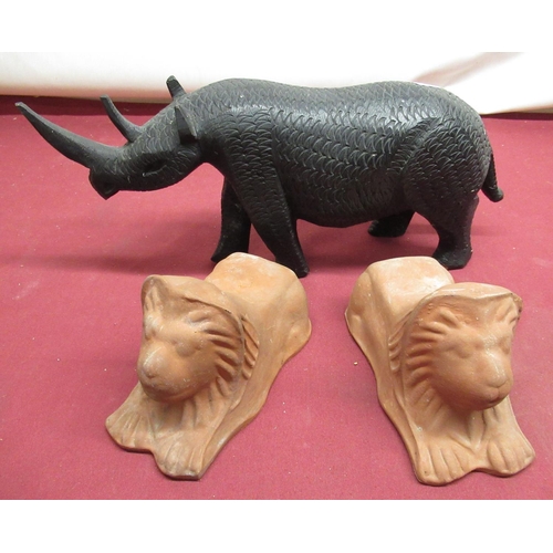 186 - Ebonised wooden model of a rhino and two terracotta lion figures (3)