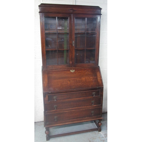 266 - C20th oak bureau-bookcase, two glazed doors and fall front above three drawers on turned supports wi... 