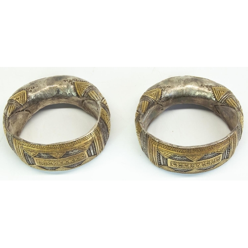 1225 - Pair of white metal Omani Ibri hollow bracelets with flat fronts embellished with gilded panels, pun... 