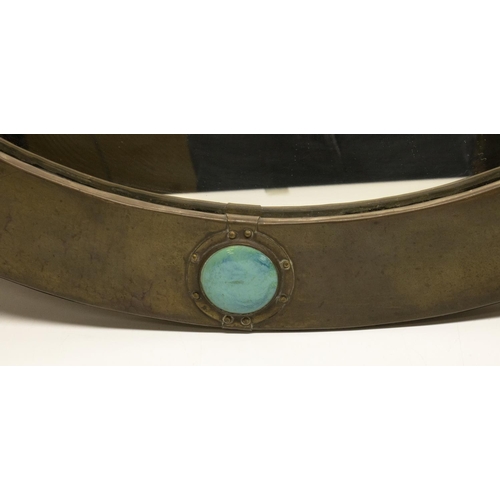 1233 - Liberty of London - a hammered brass oval mirror with nailed fold over rim, set with four Ruskin typ... 