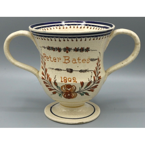 1215 - C20th Prattware loving cup painted 'Peter Bates 1802' in floral wreath, H13cm