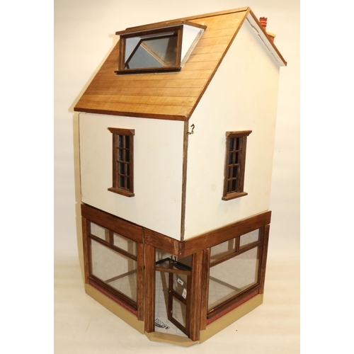 Three-room dolls house modelled as a corner shop, comprising ground floor shop front, room above, and attic room, with wall and floor coverings, and lighting, H75cm W38 D33cm