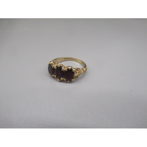 1242 - 9ct yellow gold three stone ring set with red stones, 375, stamped 375, size N, 3.2g