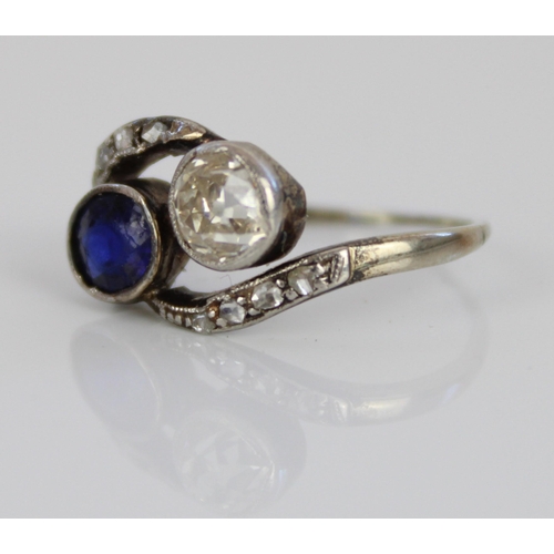 1013 - White metal diamond and sapphire crossover ring, the round cut diamond and oval cut sapphire in rub-... 