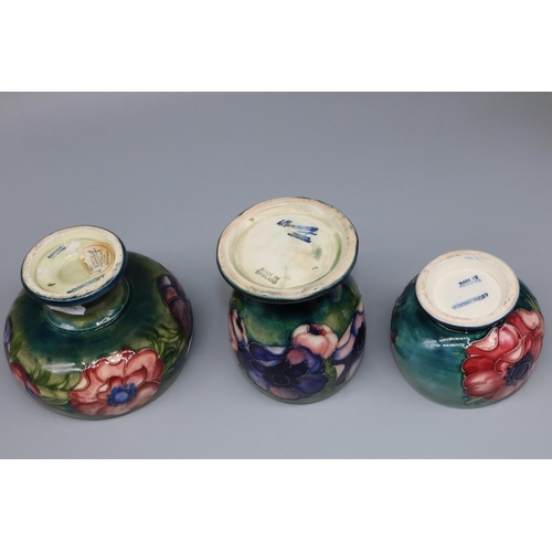 1145 - Moorcroft Pottery: three Anemone pattern vases, tubelined decoration of purple and pink flowers on g... 