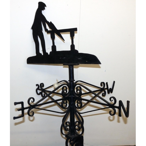 1393 - Black painted metal weather vane, with a carpenter sawing at a bench pointer on wrought metal scroll... 