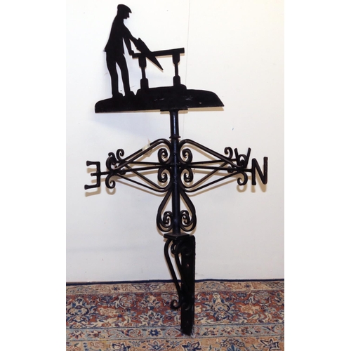 1393 - Black painted metal weather vane, with a carpenter sawing at a bench pointer on wrought metal scroll... 