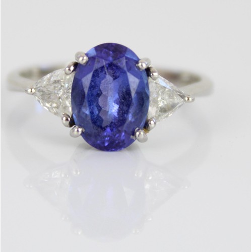 1000 - Platinum three stone tanzanite and diamond ring, the central oval cut tanzanite flanked by two trian... 
