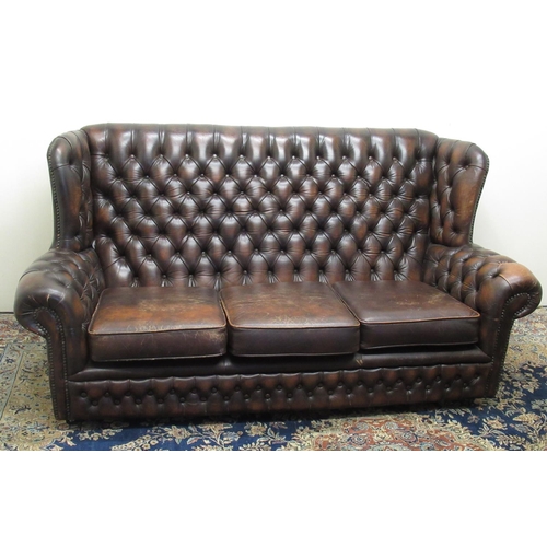 672 - Brown nailed leather wing back sofa with deep buttoned back and arms, three seat cushions, W176cm