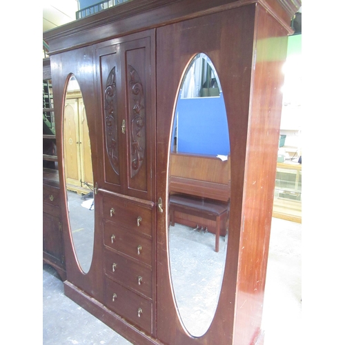 292 - Edwardian walnut triple wardrobe with carved doors and four drawers enclosed by two oval mirror door... 