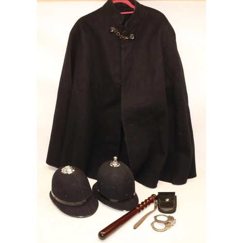 904 - Police uniform items comprising woollen cape, two helmets, truncheon, and a pair of handcuffs marked... 