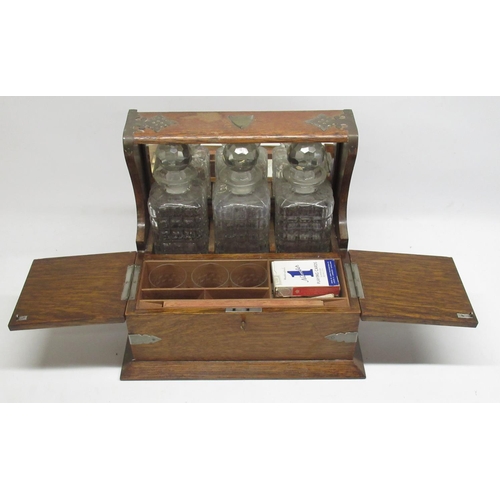 285 - Early C20th three decanter oak tantalus with plated mounts and games compartment W38cm